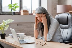 Woman sitting at desk, struggling with migraine pain